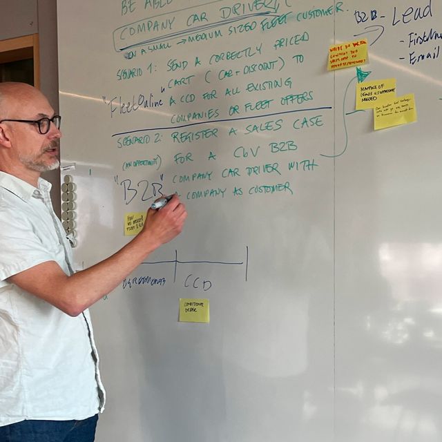 A man writes on a whiteboard during a co-creation workshop, surrounded by sticky notes and sketches.