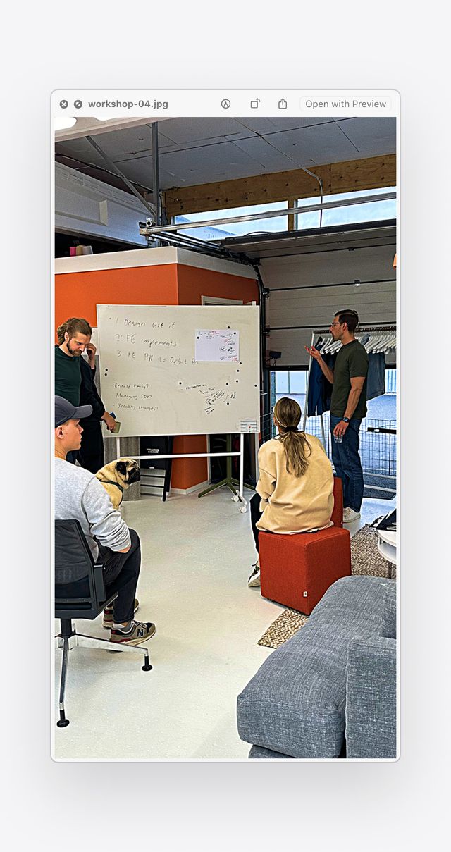 Workshop scene with a group of people and a dog gathered around a whiteboard, discussing design system implementation steps in a modern office.