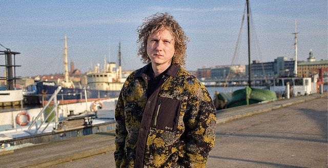 Aleksandr standing on a dock in Gothenburg harbor, wearing a patterned jacket